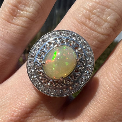 Close-up of finger wearing a double halo opal ring in natural sunlight.