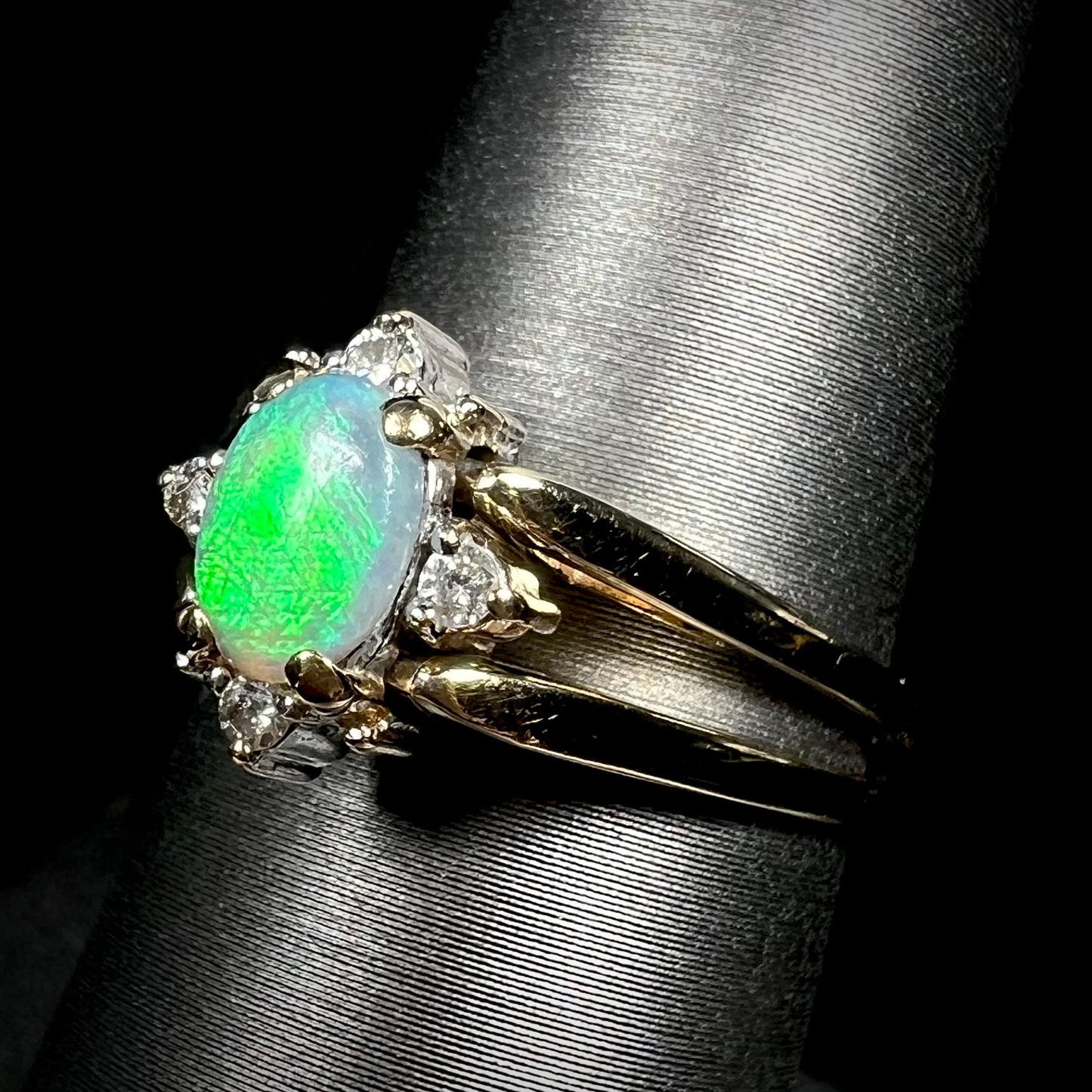 Angled close-up of double-sided opal and diamond flip ring in 14k gold, shown on ring display.  Opal has bright green flash