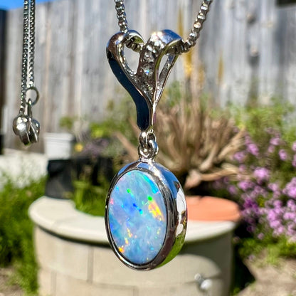 An oval cut black opal doublet necklace set in sterling silver with white zircon accent stones.