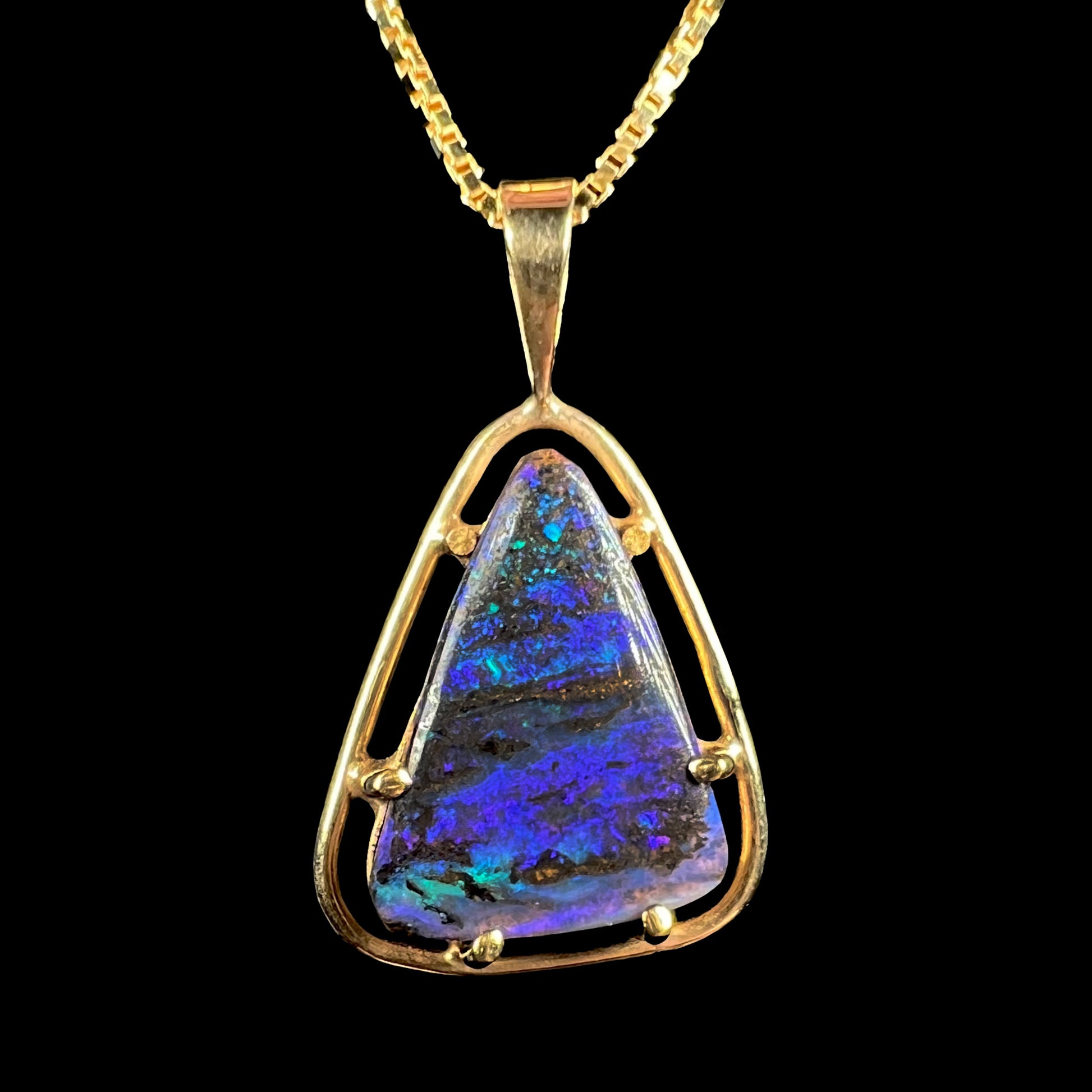 Close-up of a dainty Duck Creek opalized wood pendant in 9k gold, shown against a black background.