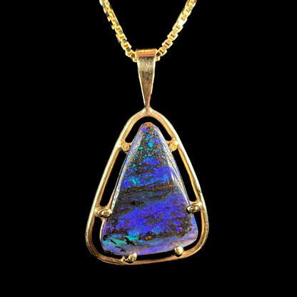 Close-up of a dainty Duck Creek opalized wood pendant in 9k gold, shown against a black background.