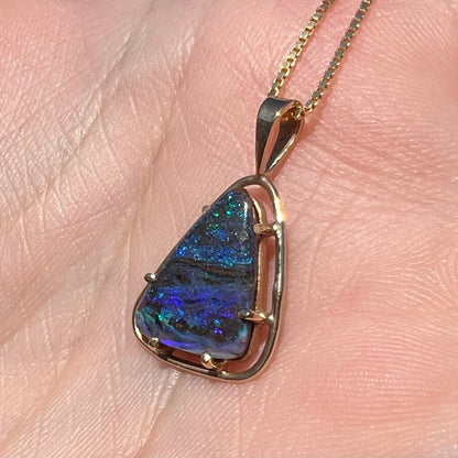 Angled close-up of a dainty Duck Creek opalized wood pendant in 9k gold, shown in the sunlight in a hand.