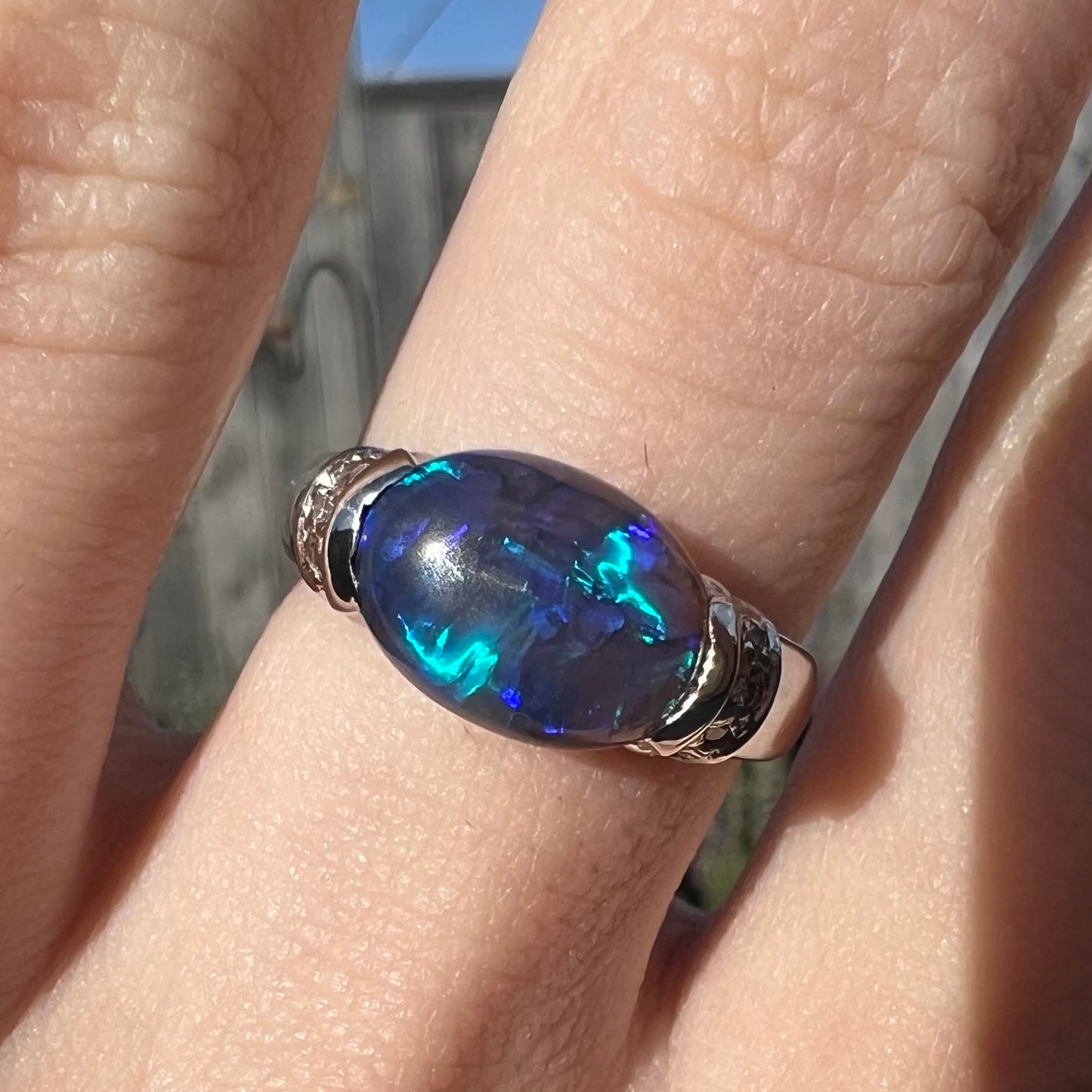 An East-West set black opal and platinum ring worn on a hand.  The ring is platinum.