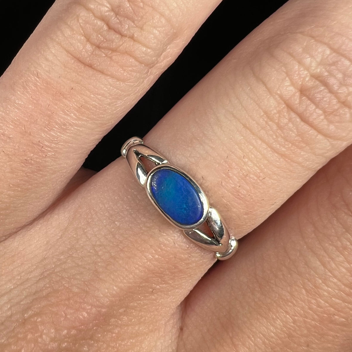 Close-up of East-West oriented bezel set opal doublet solitaire ring in sterling silver, worn on finger