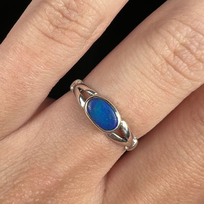 Close-up of East-West oriented bezel set opal doublet solitaire ring in sterling silver, worn on finger