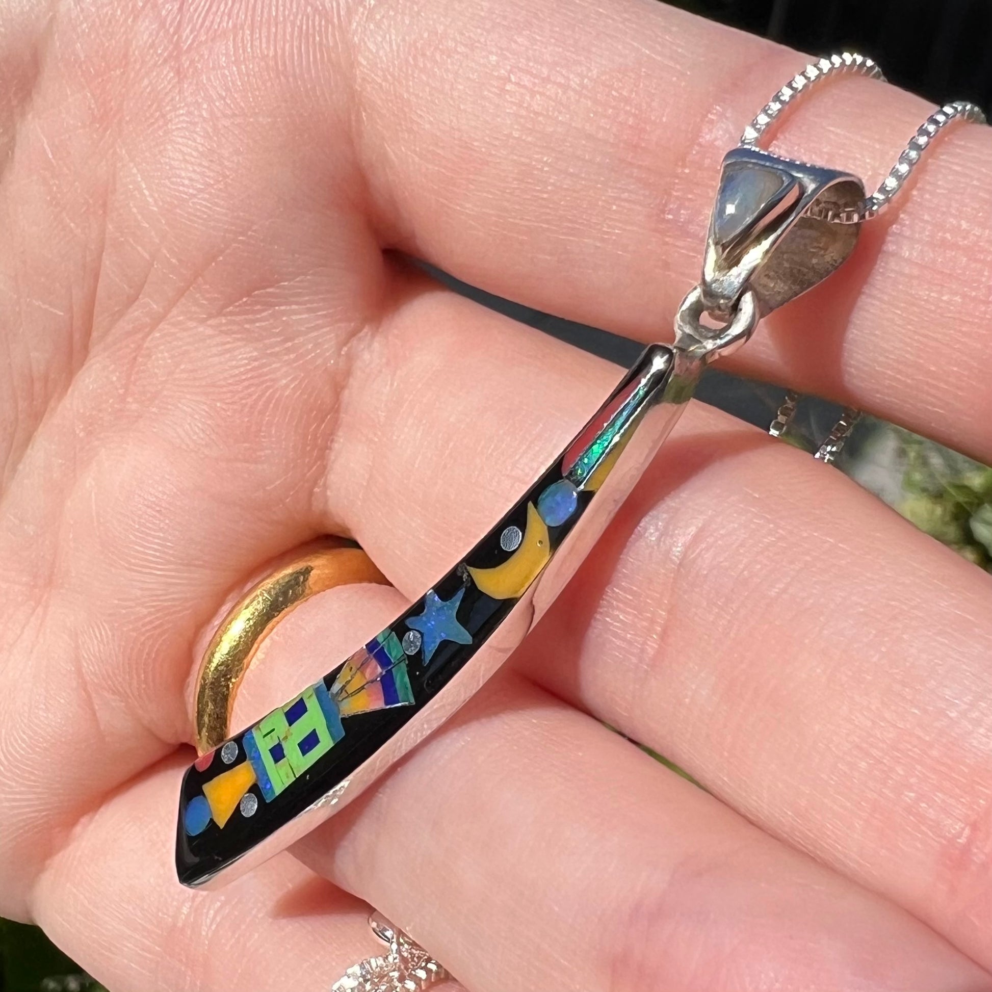 Elongated silver opal and black onyx inlay pendant shown close-up from angle in hand in natural light.