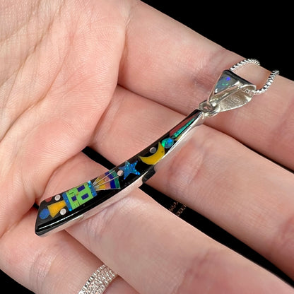 Angled close-up of an elongated Southwest-style space-inspired gemstone onyx inlay pendant held in hand under studio lights.