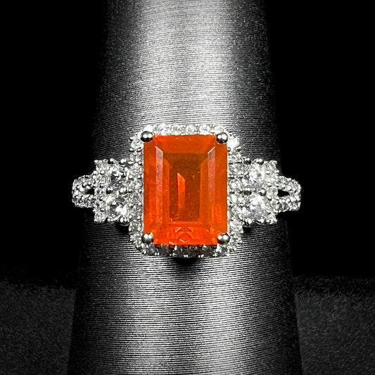 Macro shot of a white gold halo ring set with an orange emerald cut Mexican fire opal on a ring display against a black background.