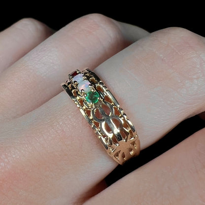 Angled view of a gold woven-style mother's ring set with two opals, an emerald, and a garnet worn on a finger.