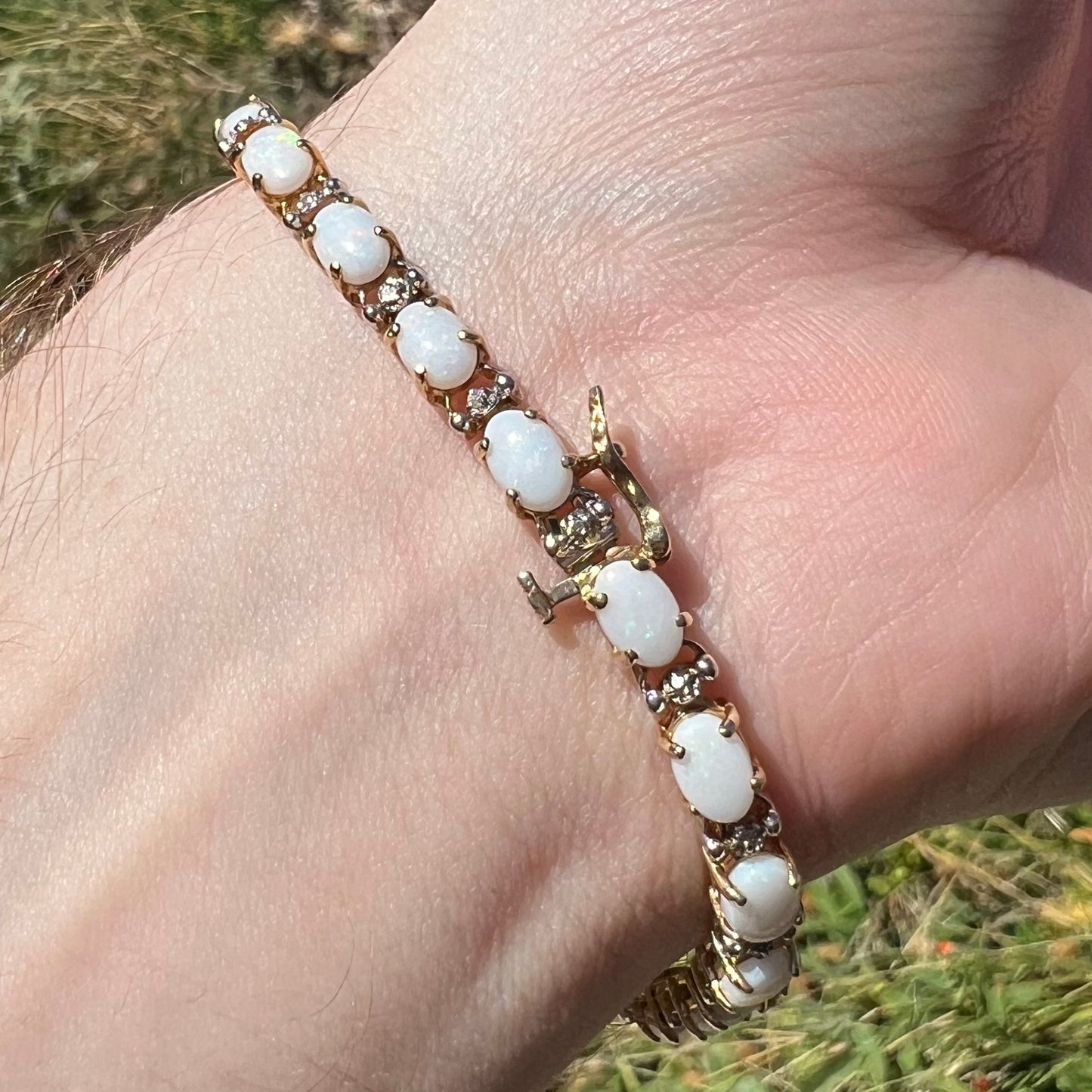 Back side of wrist wearing an estate 10k yellow gold opal and diamond bracelet in sunlight.  The bracelet's box clasp is in view.