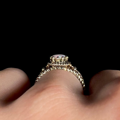 Side profile gallery view of estate brass opal ring, worn on finger; the ring has a twisted rope-design shank with many prongs holding the opal that resemble spikes of a crown