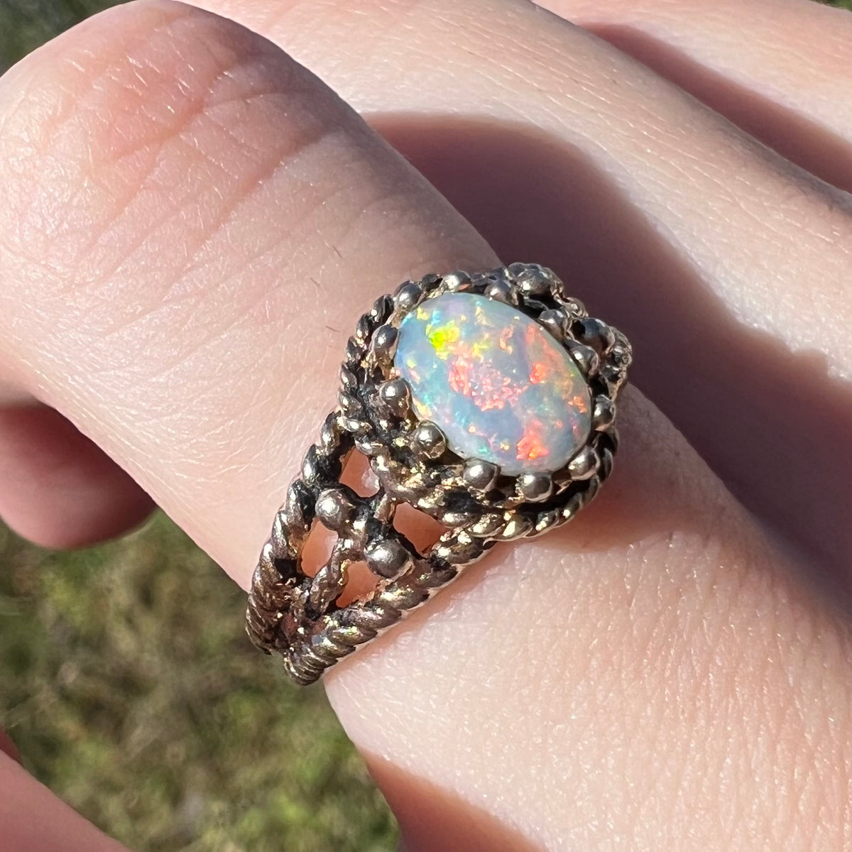 An estate base metal ring set with a colorful Australian opal, shown close-up from an angle on a finger in sunlight