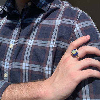 Close-up of a person resting their hand on their opposing shoulder in the sunlight while wearing an estate 14k gold opal, lapis lazuli, and diamond ring.