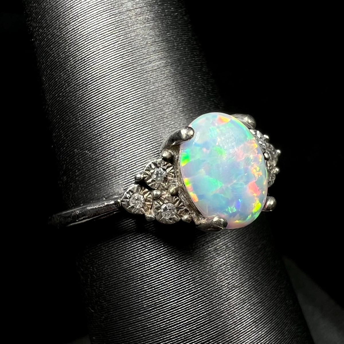 An estate sterling silver lab-created opal ring with three illusion-set diamond accents, viewed from the shoulder angle close-up.