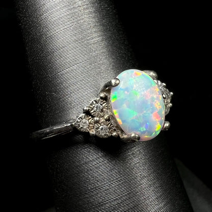An estate sterling silver lab-created opal ring with three illusion-set diamond accents, viewed from the shoulder angle close-up.