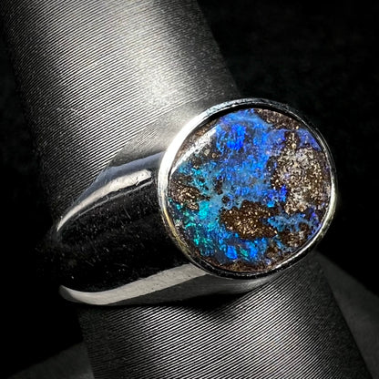 A stainless steel men's Australian boulder opal ring with blue color play, shown on a ring display from an angle.