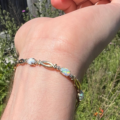Estate modernist style yellow gold bracelet set with colorful lab-created opals worn on wrist in sunlight, shown from wrist's underside.