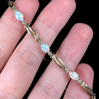 Modernist style estate opal tennis bracelet in 10k yellow gold with open links drapped over fingers.
