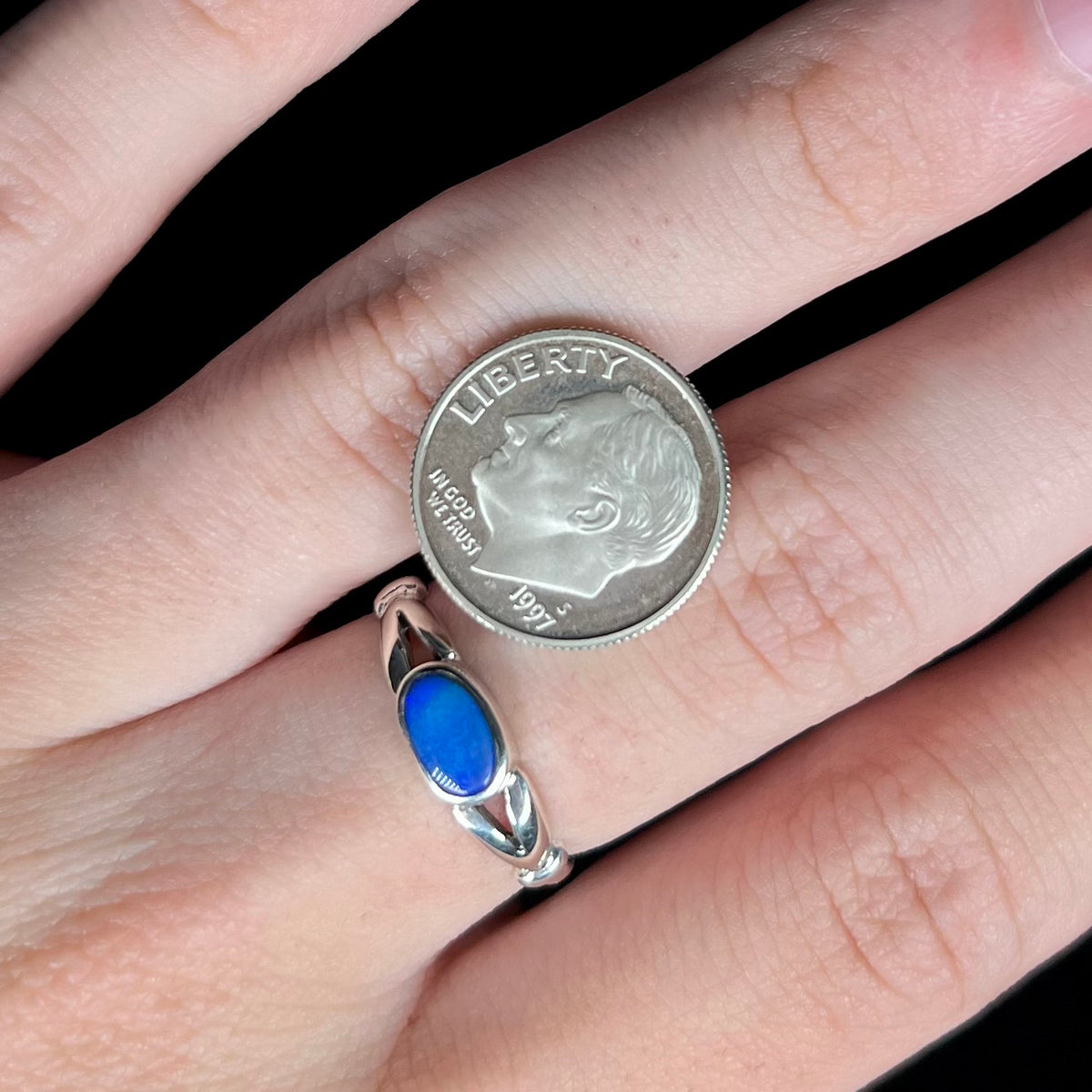 Close-up of hand wearing estate silver opal doublet ring with split shank design next to US dime coin