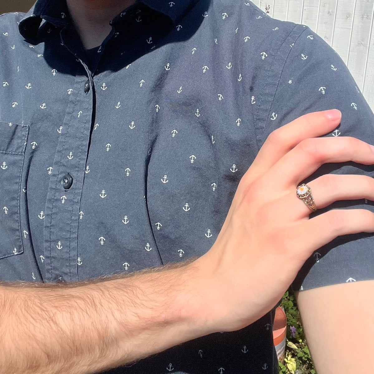 Close-up of person resting hand on opposing shoulder in sunlight while wearing an estate brass opal ring; the natural Australian opal has a red flash of color