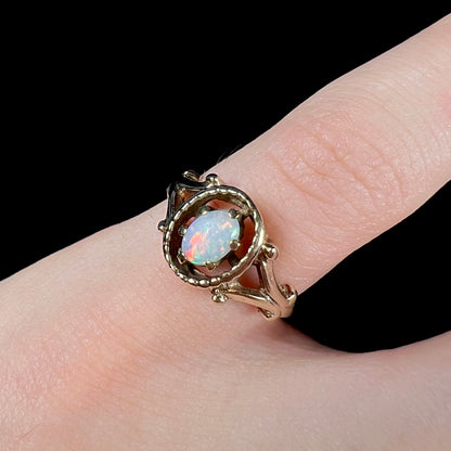 A ladies' Art Nouveau style opal solitaire ring.  The mounting is yellow gold with filigree accents.