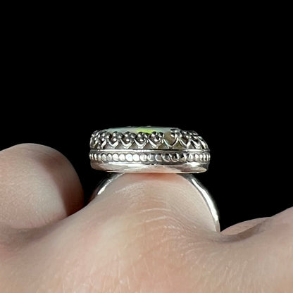 Side gallery view of an estate sterling silver opal ring with a crown design, worn on a hand against black background.