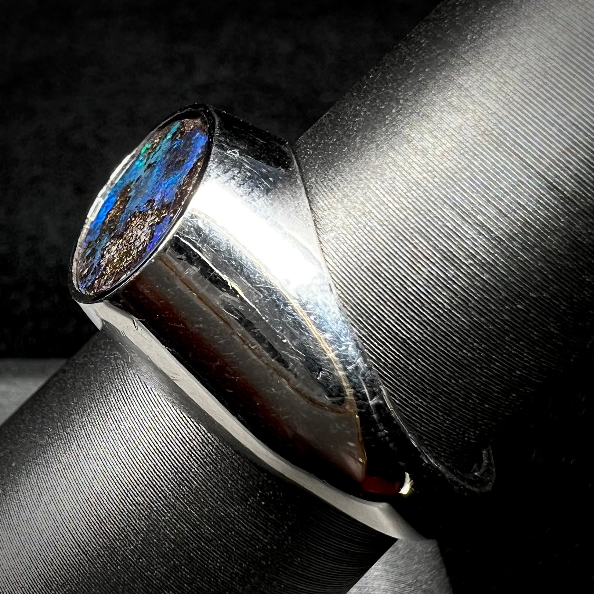 An estate men's Australian boulder opal ring with blue color play, shown on a ring display from the side.