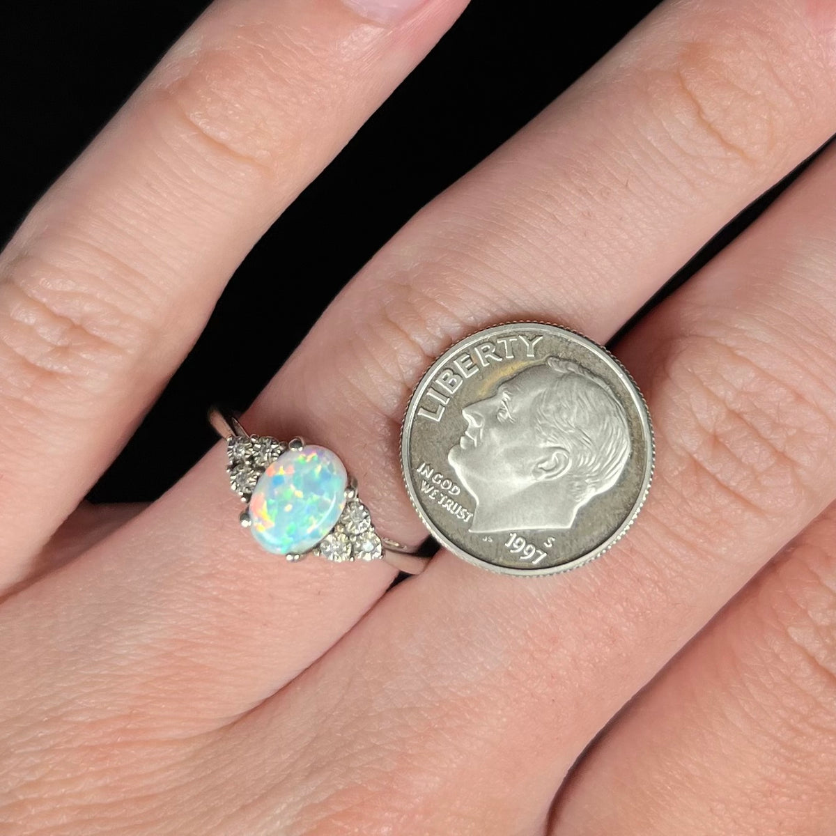 Close-up of hand wearing an estate sterling silver opal and diamond women's ring next to a US dime coin for scale.