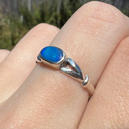 Sunlit angled close-up of estate sterling silver opal ring, worn on finger.  The blue opal has a dulled surface texture