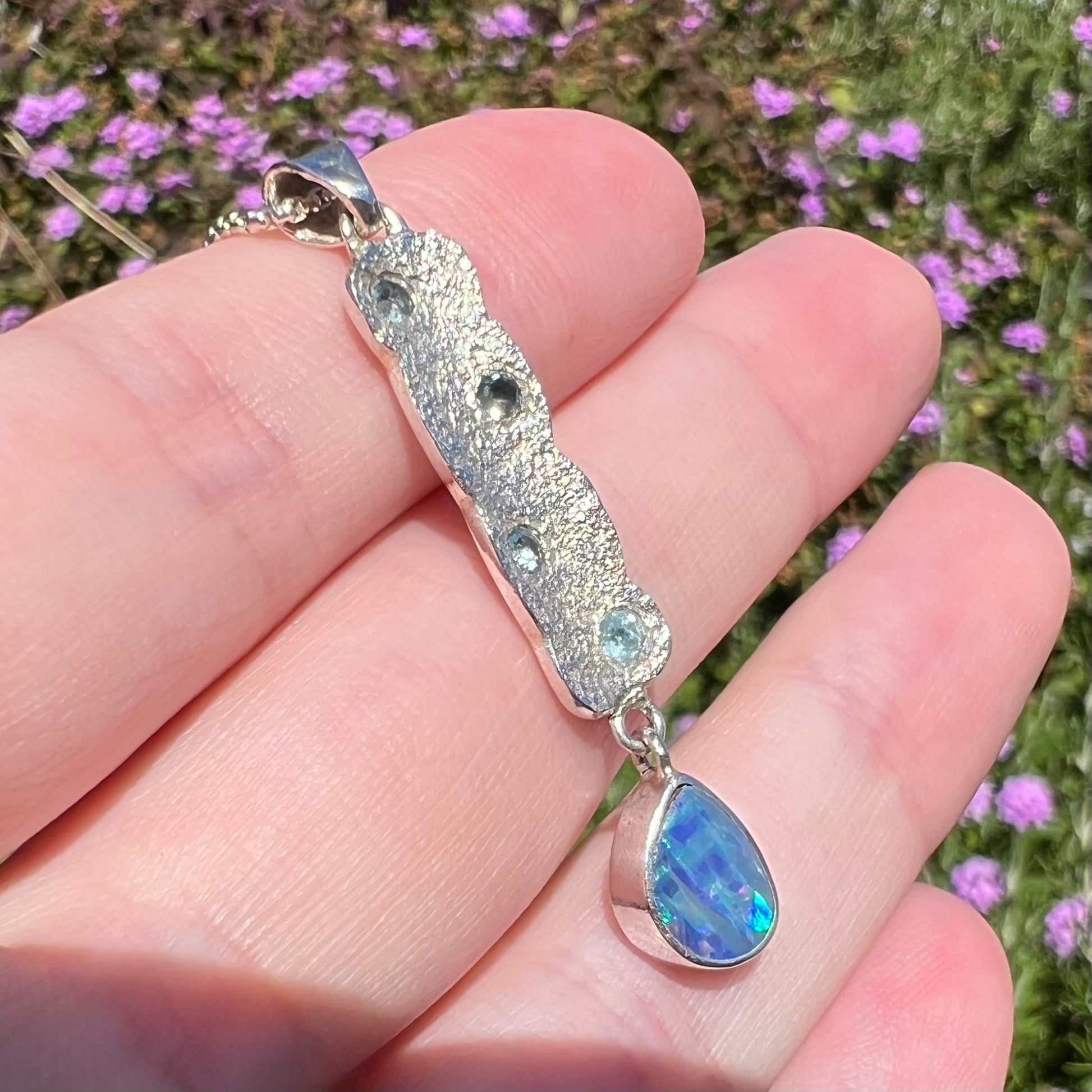 Angled macro view of an estate sterling silver Australian opal doublet and topaz-accented pendant in sunlight.