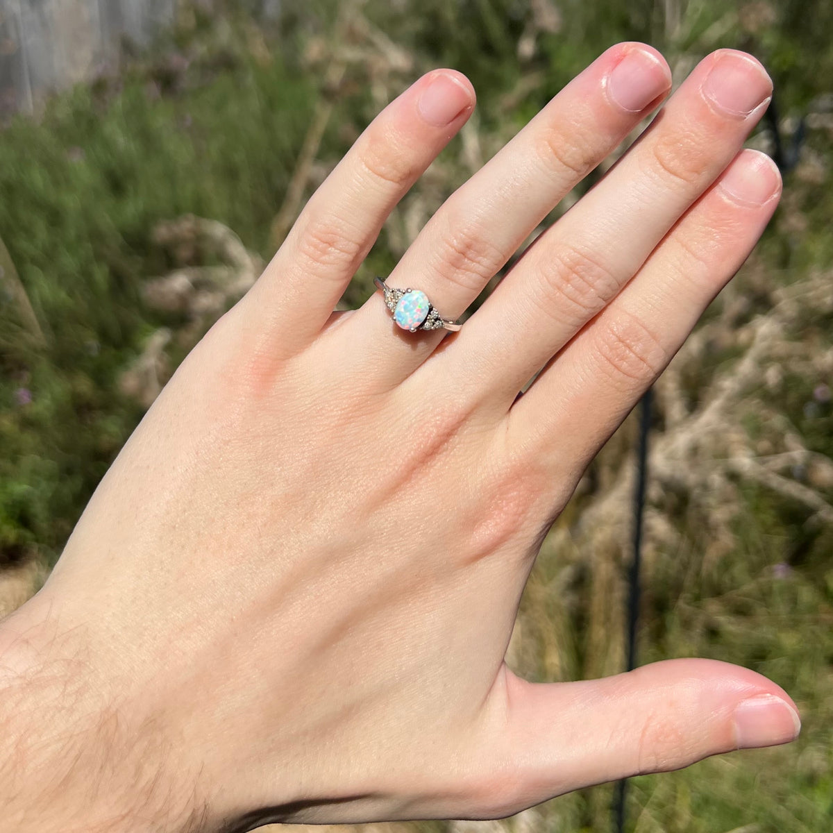 Hand wearing a women's lab-created opal and diamond ring in sunlight.