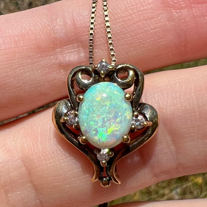 Macro close-up of a vintage 1990s Victorian-style pendant featuring ethically-sourced lab-created opal and CZ accents, shown resting on fingers in the sunlight.
