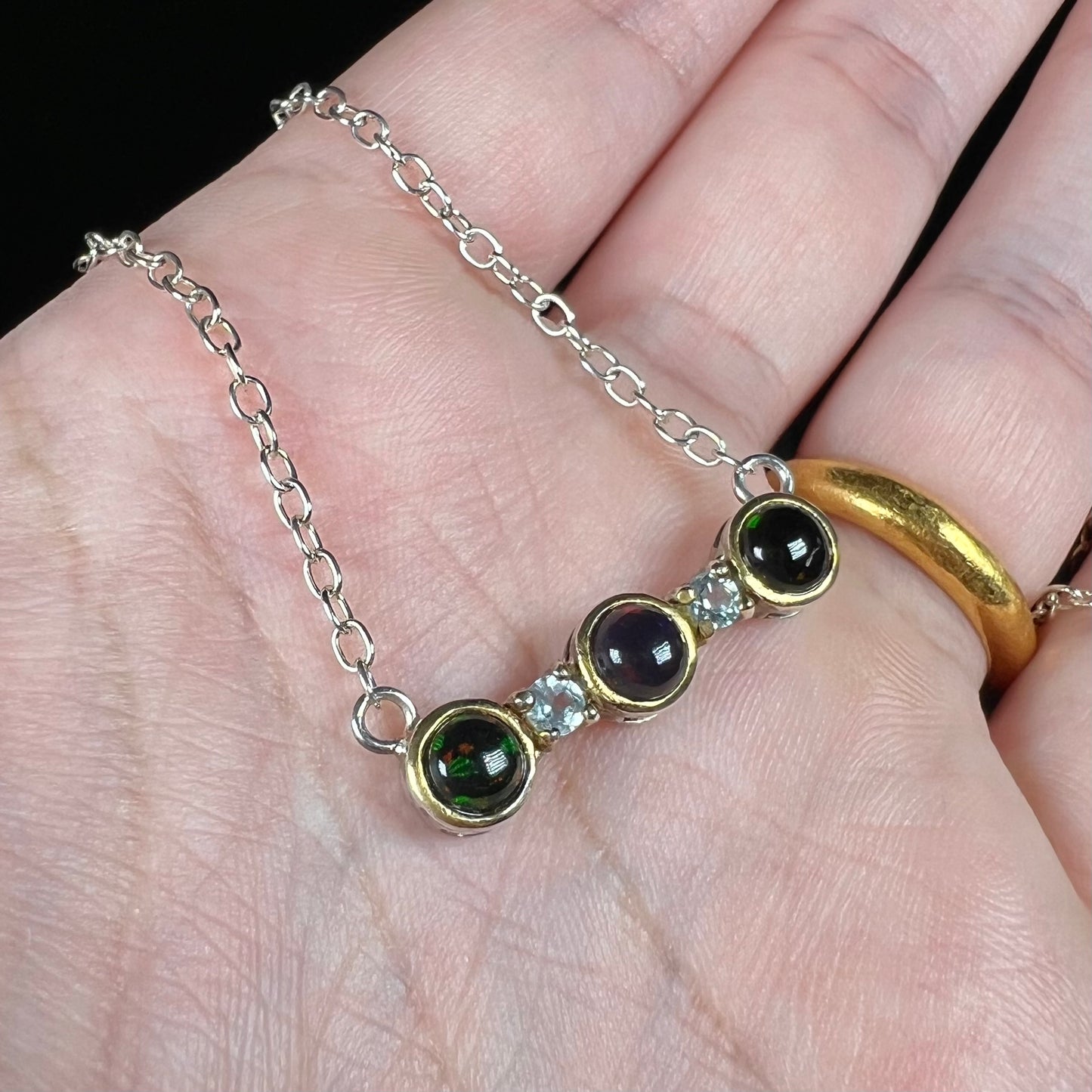 A three-stone black Ethiopian opal and white topaz necklace in two-tone sterling silver.