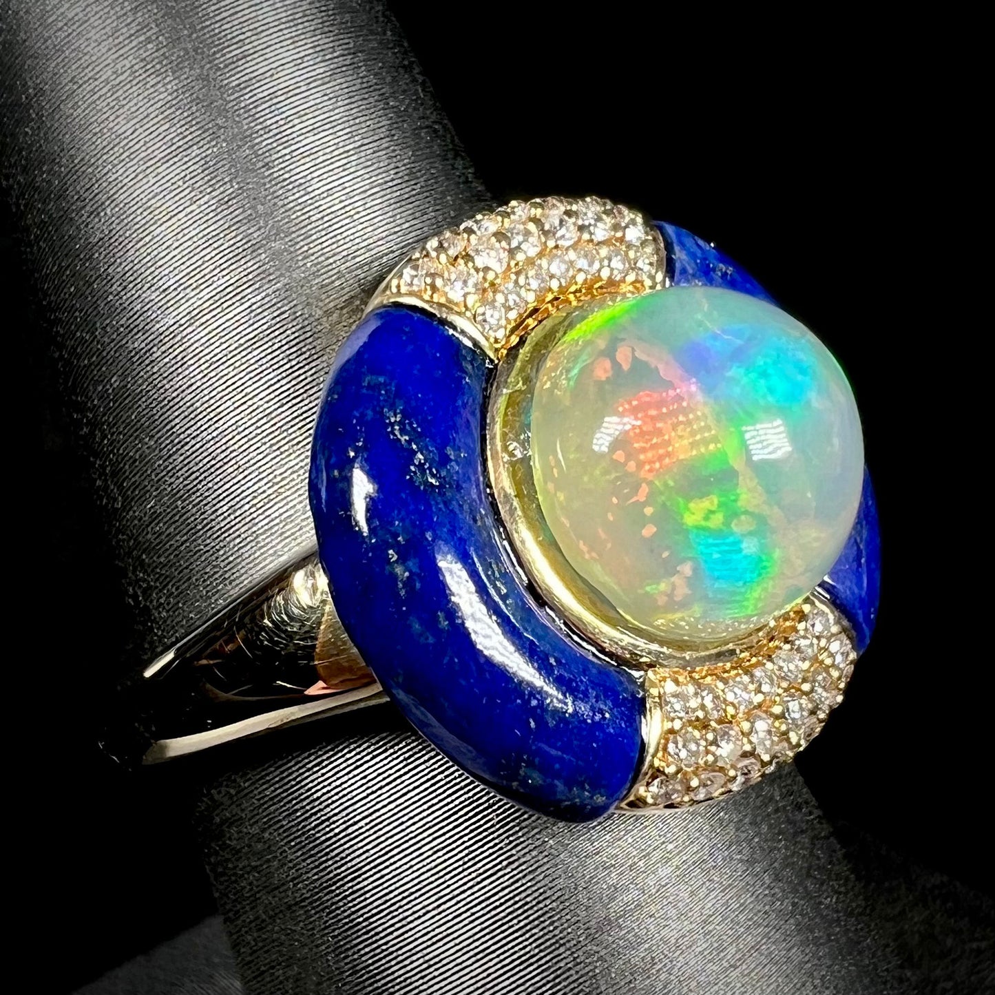 A women's Ethiopian fire opal, lapis lazuli, and diamond ring in 14k yellow gold, shown from an angled close-up view on a ring display.