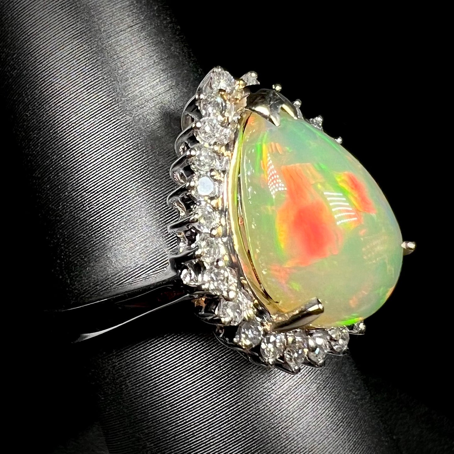 An Ethiopian fire opal and diamond halo ring in white gold, shown close-up from an angle.  The opal has a red flash of color.