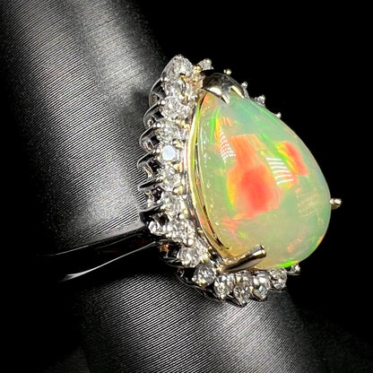 An Ethiopian fire opal and diamond halo ring in white gold, shown close-up from an angle.  The opal has a red flash of color.