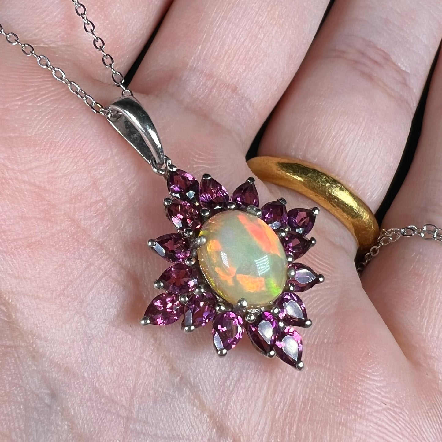 A sterling silver Ethiopian opal and rhodolite garnet spray necklace shown in a hand at an angle with red color play.