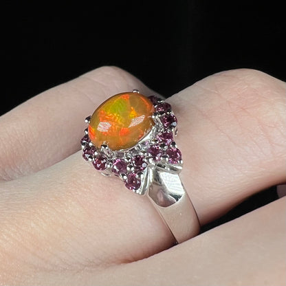 Angled close-up of sterling silver Ethiopian opal fire opal and garnet ring, worn on finger