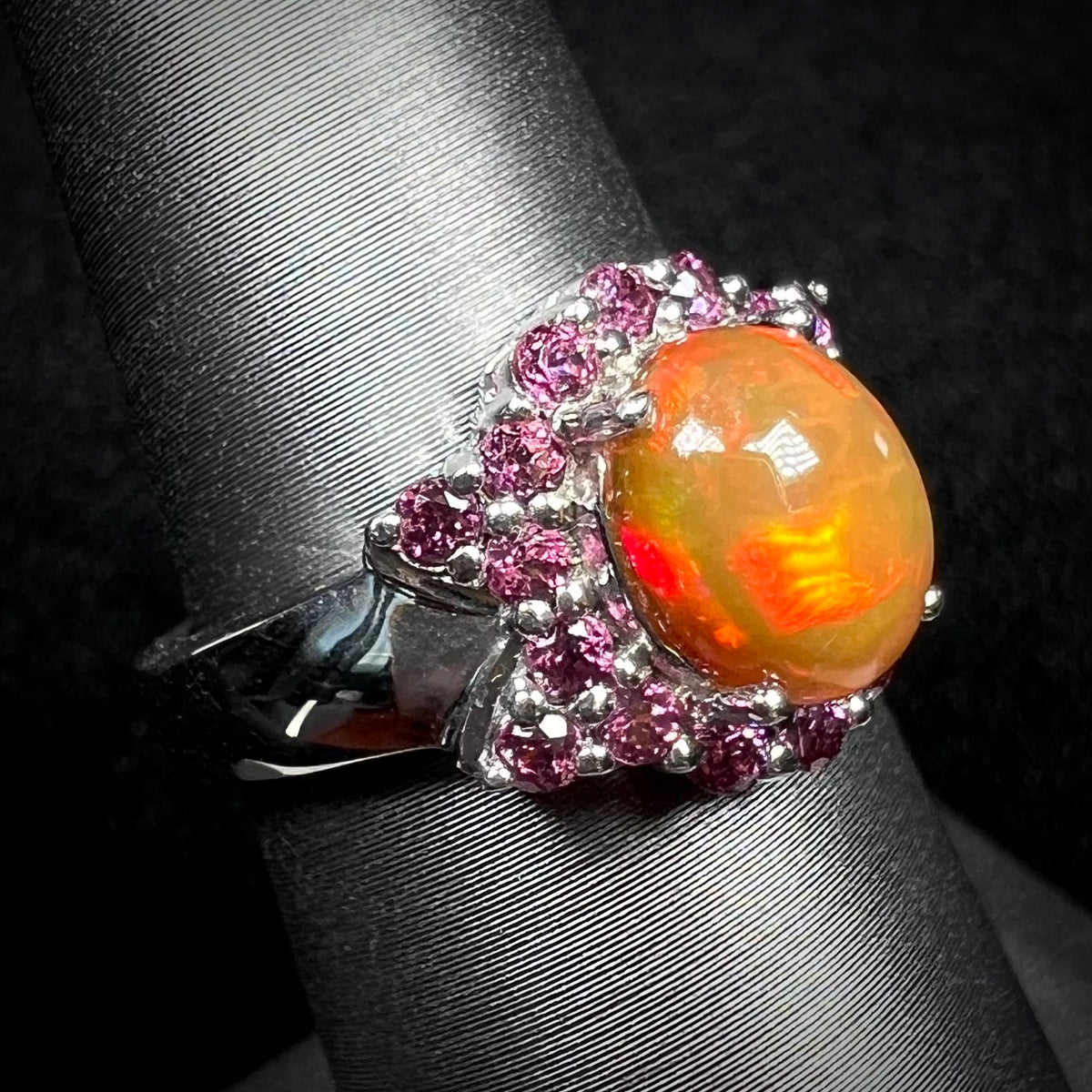 Burnt orange colored Ethiopian fire opal and purple rhodolite garnet ring in silver on display, viewed from angle