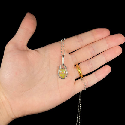 A colorful sterling silver Ethiopian fire opal necklace held in a hand against a black background.
