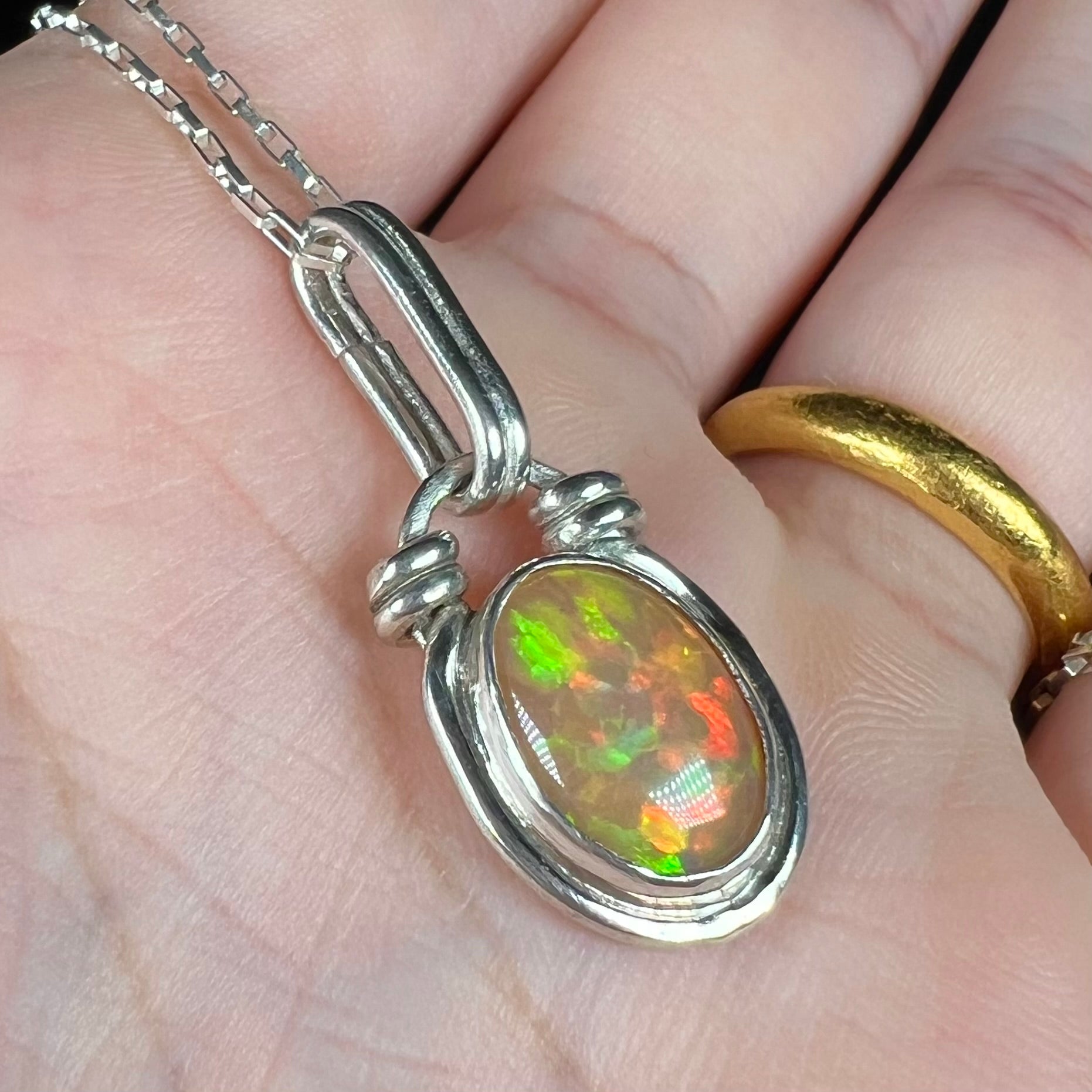 A sterling silver Ethiopian fire opal pendant shown in a hand close-up from an angle.