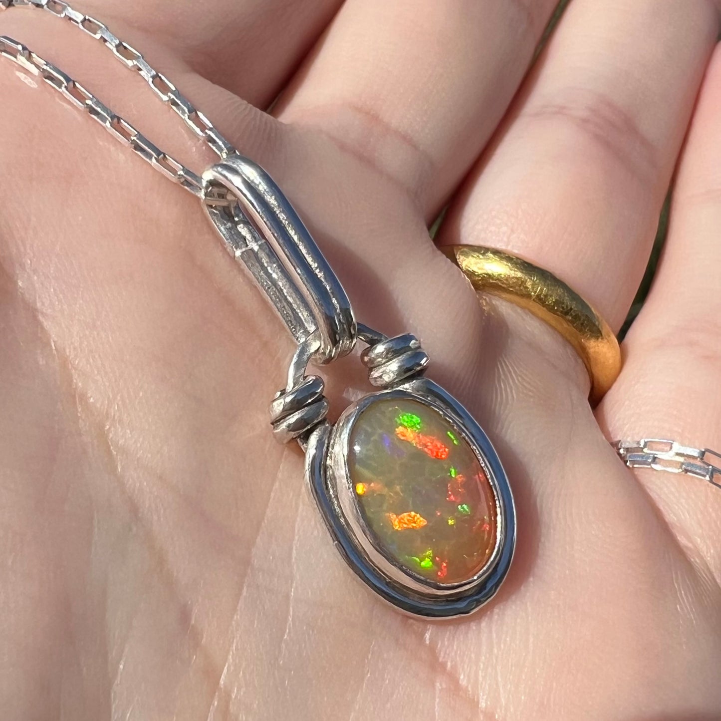 Angled close-up of a colorful sterling silver Ethiopian opal pendant, held in the sunlight.