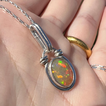 Angled close-up of a colorful sterling silver Ethiopian opal pendant, held in the sunlight.