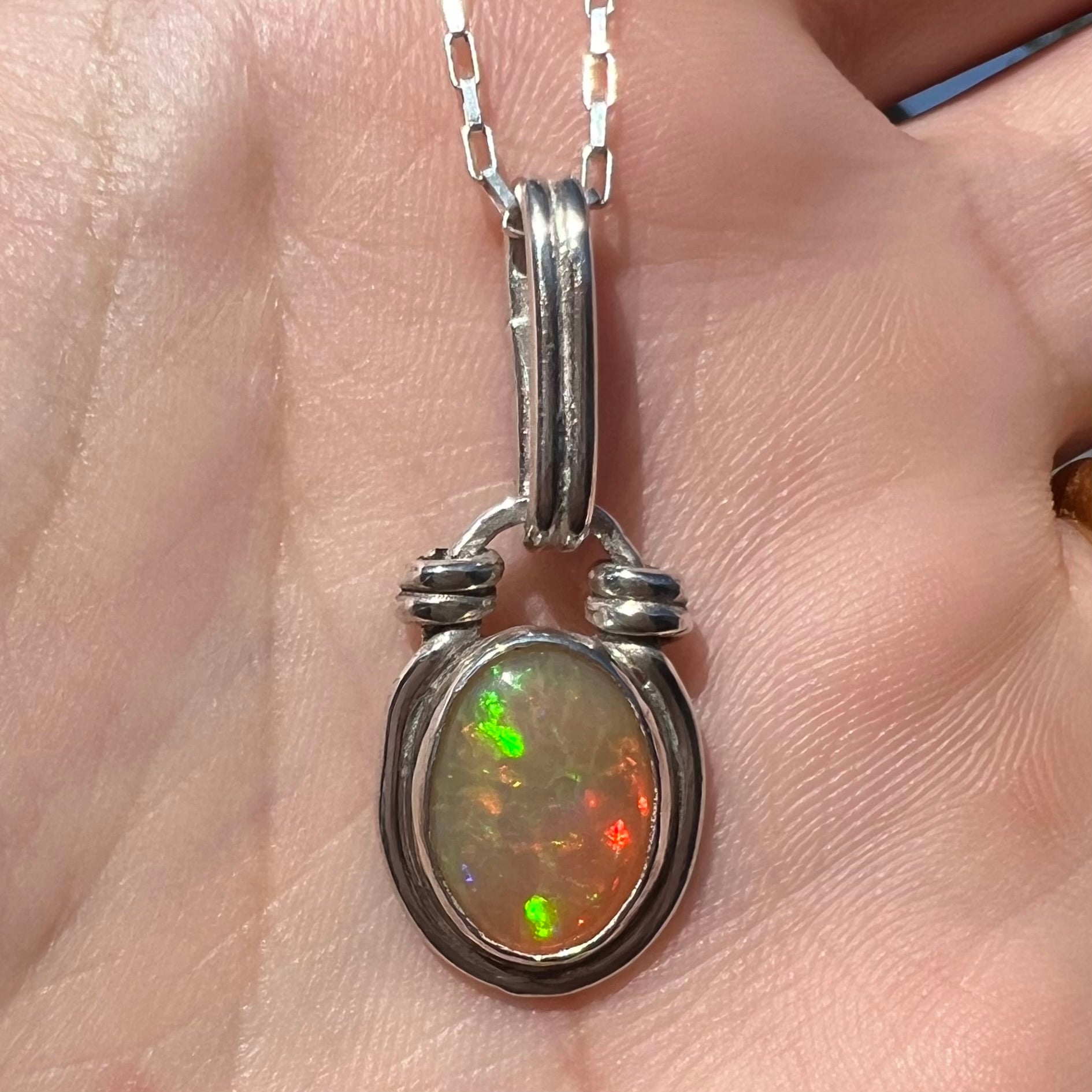 Close-up of a colorful sterling silver Ethiopian opal pendant in sunlight, held in a hand.