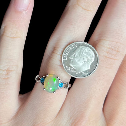 Silver Ethiopian opal and blue apatite ring on hand next to US dime coin for scale