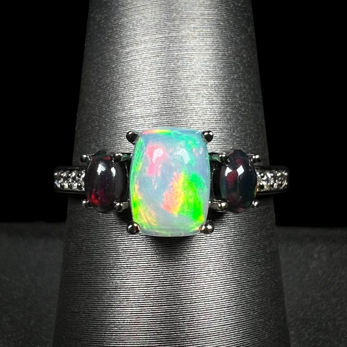 Close-up of three-stone Ethiopian opal and cubic zirconia-accented ring with black rhodium finish, shown on ring display