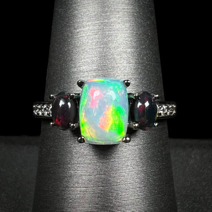 Close-up of three-stone Ethiopian opal and cubic zirconia-accented ring with black rhodium finish, shown on ring display