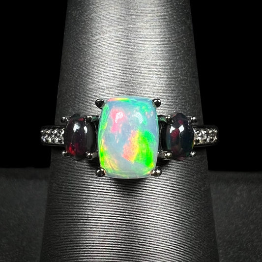 Close-up of three-stone Ethiopian opal and cubic zirconia-accented ring with black rhodium finish, shown on ring display