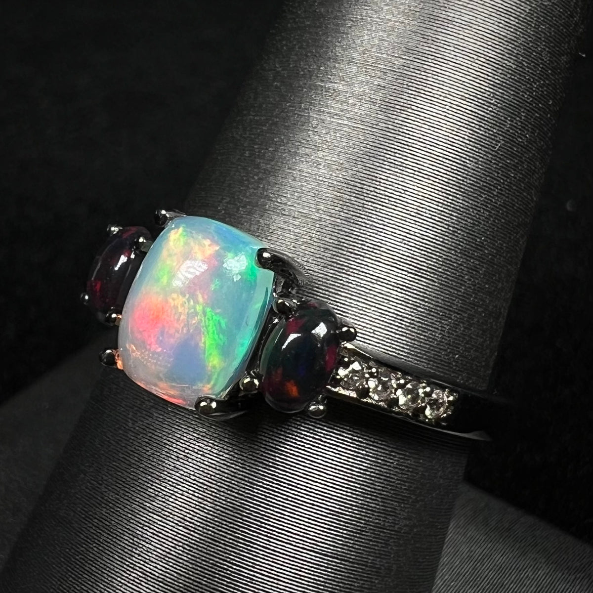 Angled close-up of three-stone opal ring with black smoked Ethiopian opals and CZ accents, shown on ring display