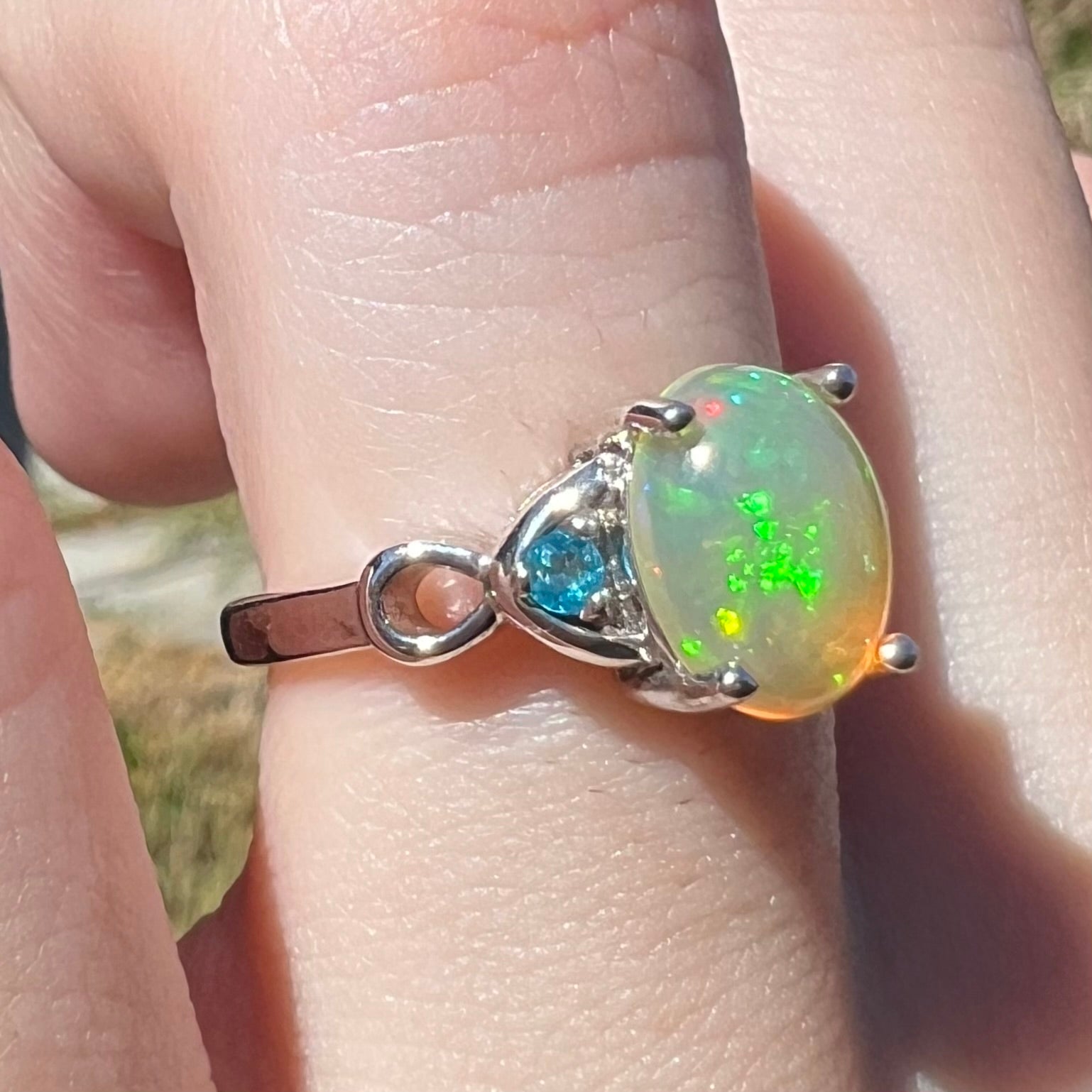 Ethiopian opal ring with green flashes and blue apatite accents in silver shown in sunlight on finger